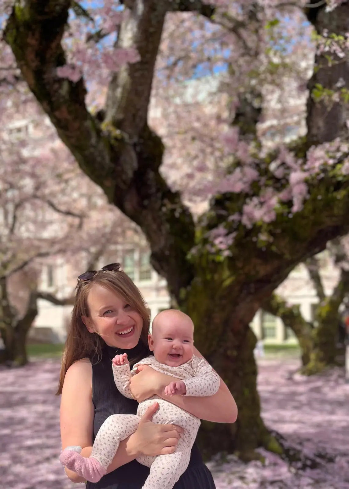 Woman holding a baby in front of cherry blossom trees