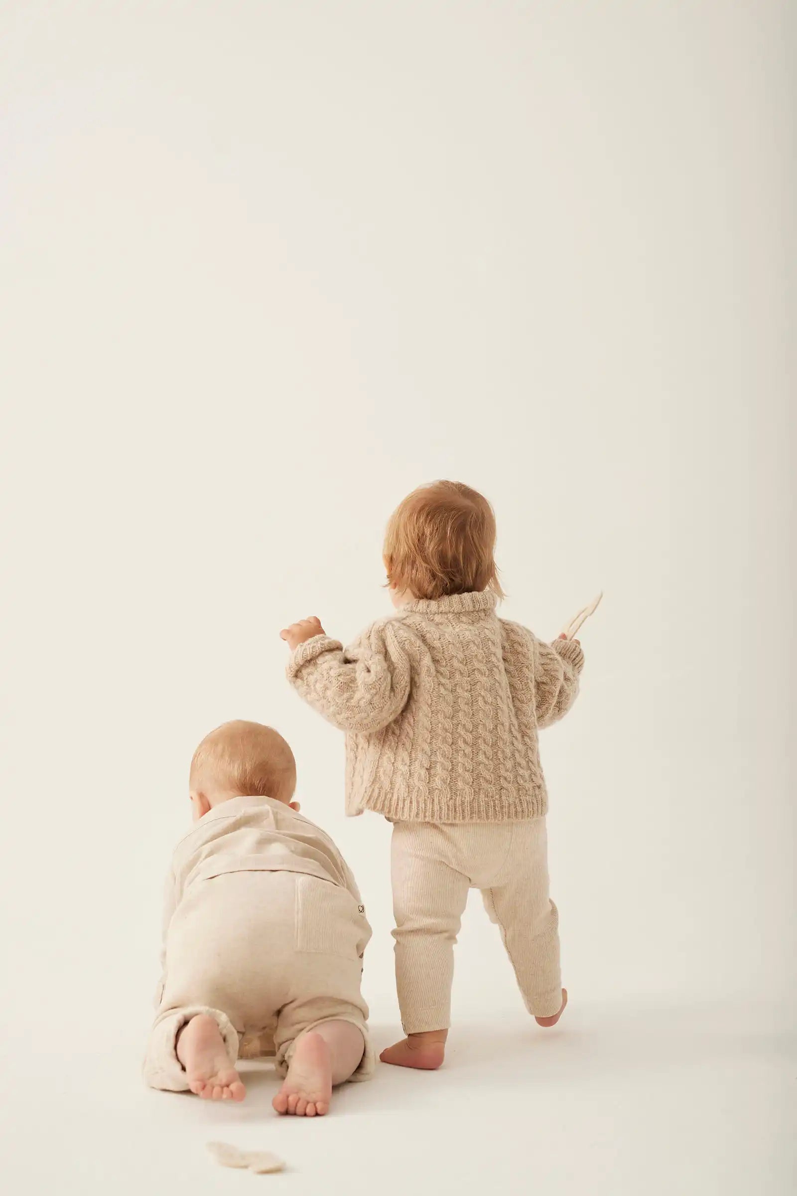 Two children in matching beige outfits standing on a white background